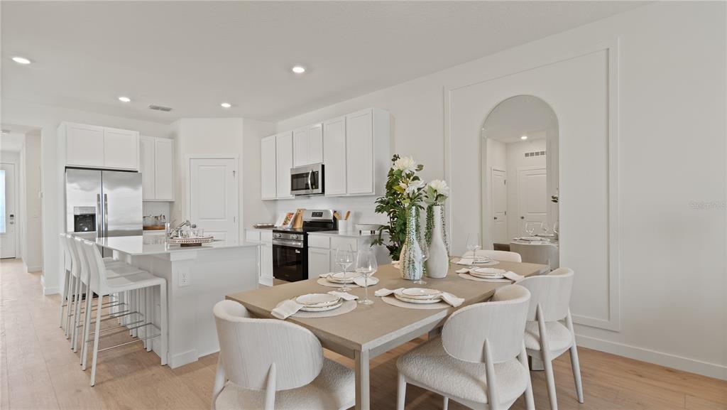 A kitchen with white cabinets and an island next to a dining area with chairs — 5395 WHISPERING GARDEN WAY, CLERMONT, FL