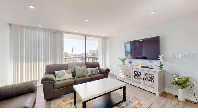 A living room features a brown sofa, a white coffee table, and a wall-mounted television — 400 ISLAND WAY UNIT 210, CLEARWATER BEACH, FL