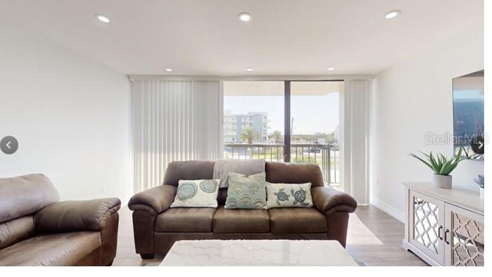 A living room with a brown sofa, a side chair, and a sliding glass door — 400 ISLAND WAY UNIT 210, CLEARWATER BEACH, FL