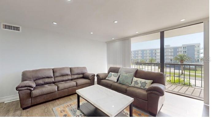 A living room features two brown sofas, a white coffee table, and a sliding glass door — 400 ISLAND WAY UNIT 210, CLEARWATER BEACH, FL