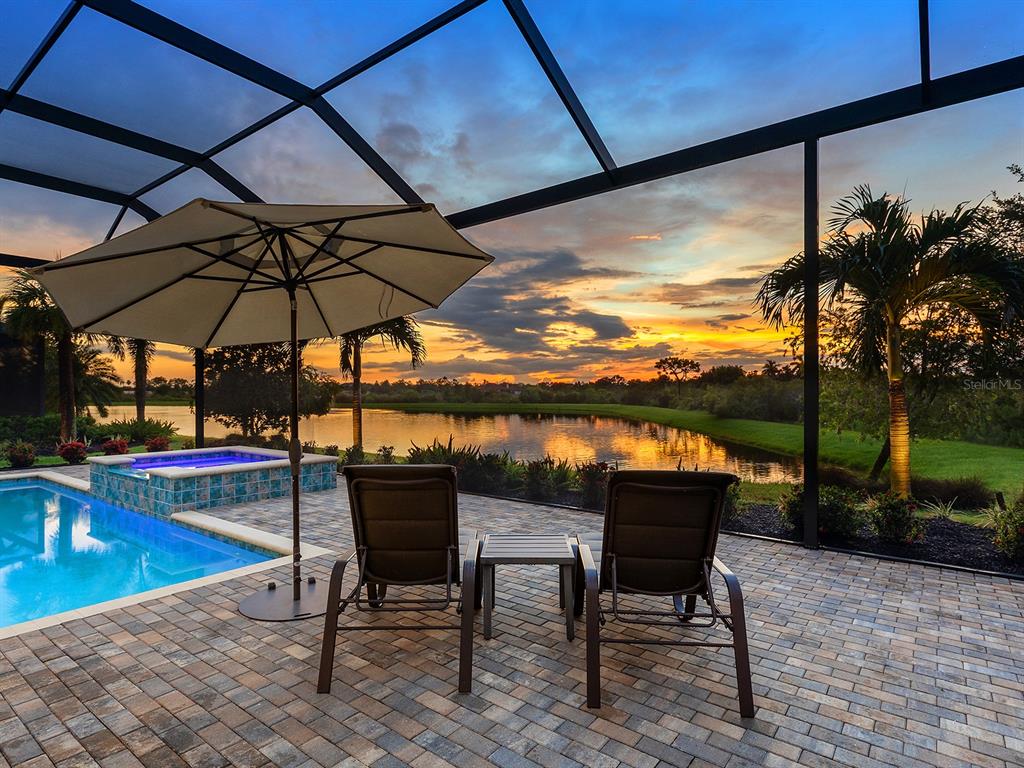 A patio with a pool, hot tub, and lounge chairs overlooks a lake at sunset — 16739 VERONA PLACE, LAKEWOOD RANCH, FL