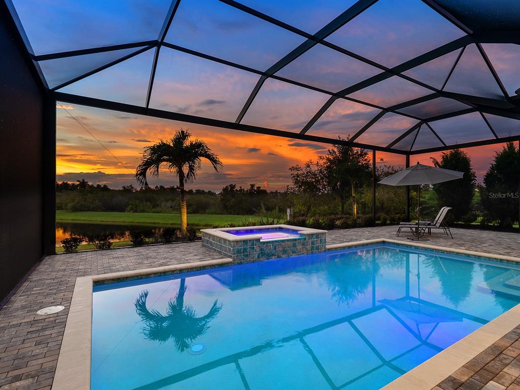 A swimming pool and spa sit inside a screened lanai overlooking a sunset landscape — 16739 VERONA PLACE, LAKEWOOD RANCH, FL