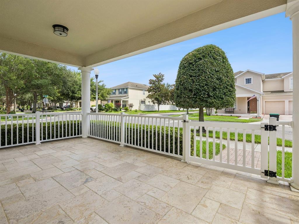 A covered patio features light-colored stone flooring and a white vinyl fence with a gate — 13403 RIGGS WAY, WINDERMERE, FL