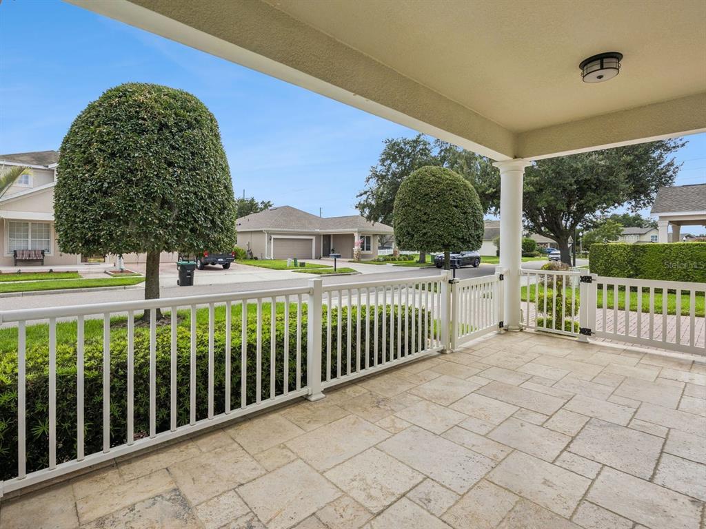 A covered stone patio features a white vinyl fence and gate overlooking a suburban street — 13403 RIGGS WAY, WINDERMERE, FL