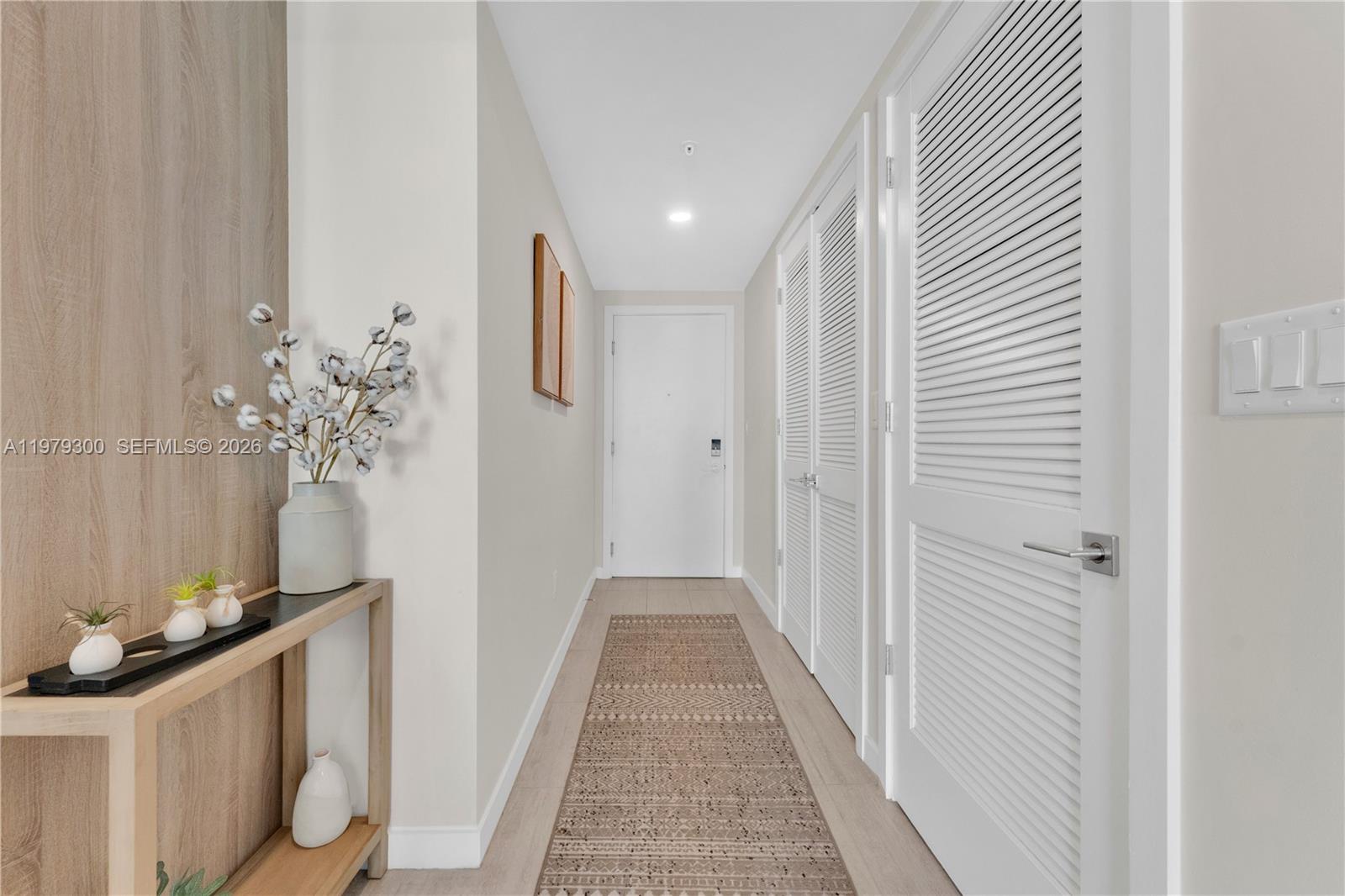 A hallway features light wood flooring, a patterned runner, and white louvered closet doors — 3900 Biscayne Blvd # 916, Miami FL 33137, MIAMI, FL