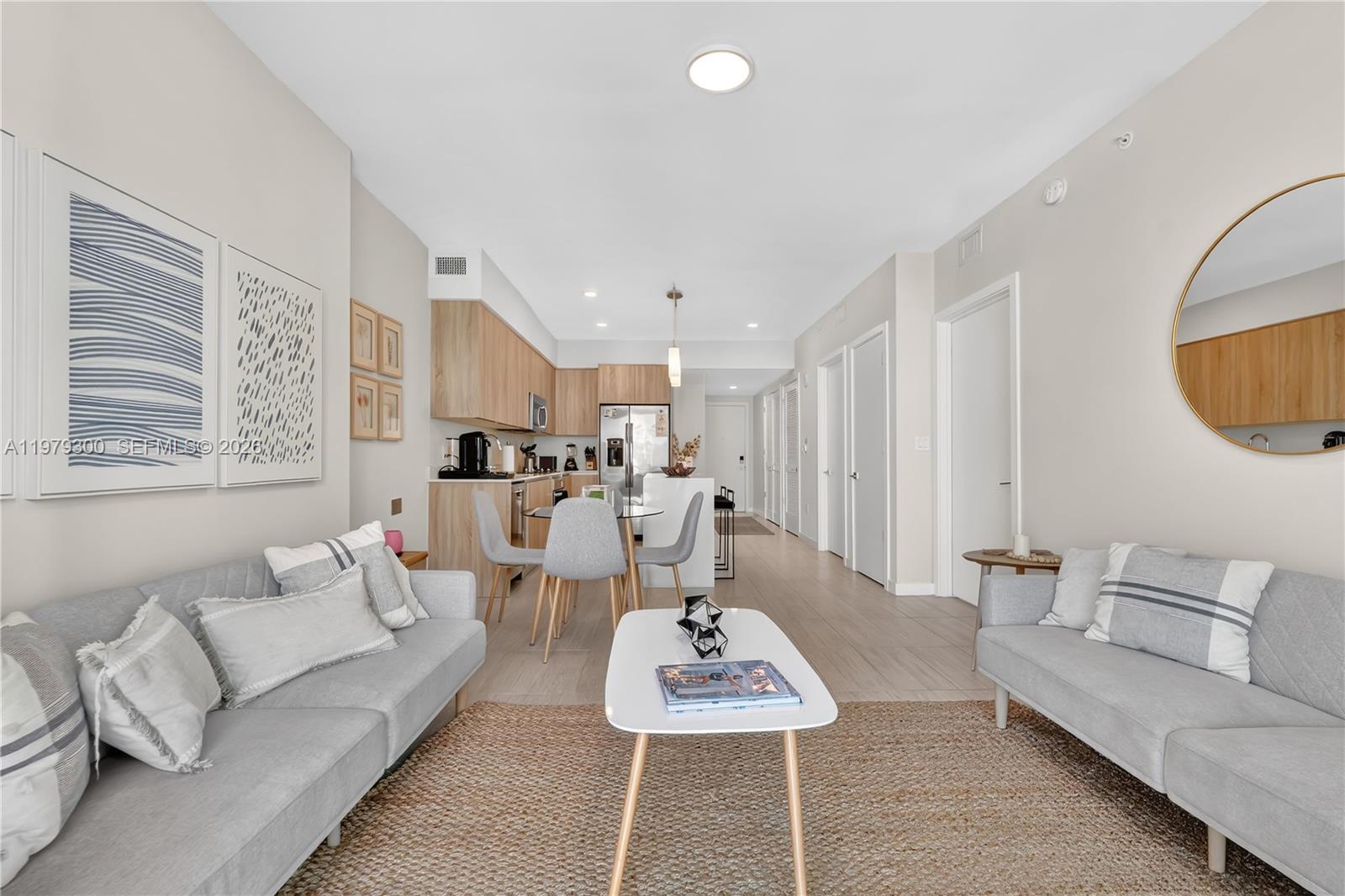 A modern living room and kitchen area features light wood cabinets, gray sofas, and tile flooring — 3900 Biscayne Blvd # 916, Miami FL 33137, MIAMI, FL