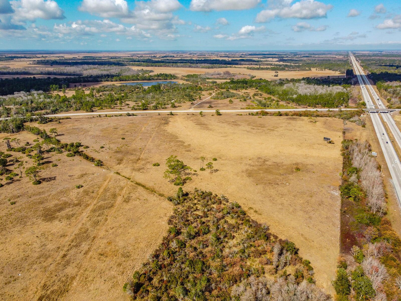 An aerial view shows a large, dry, grassy field bordered by a highway and trees — 5001 S Kenansville Road, Okeechobee FL 34972, OKEECHOBEE, FL