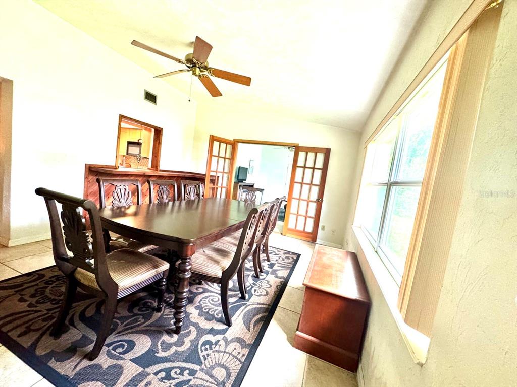 A dining room features a dark wood table, patterned rug, ceiling fan, and French doors — 49 LAUREL OAKS CIRCLE, ORMOND BEACH, FL