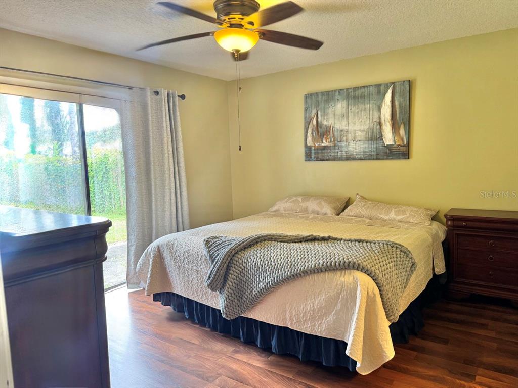A bedroom features a bed with a knit throw, wood flooring, and a sliding glass door — 49 LAUREL OAKS CIRCLE, ORMOND BEACH, FL