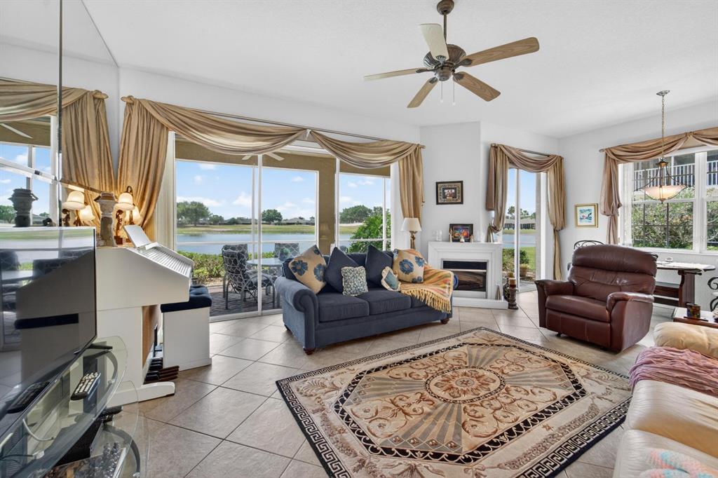 A living room features tile floors, a blue sofa, a brown recliner, and lake views — 1364 EMERALD DUNES DRIVE, SUN CITY CENTER, FL