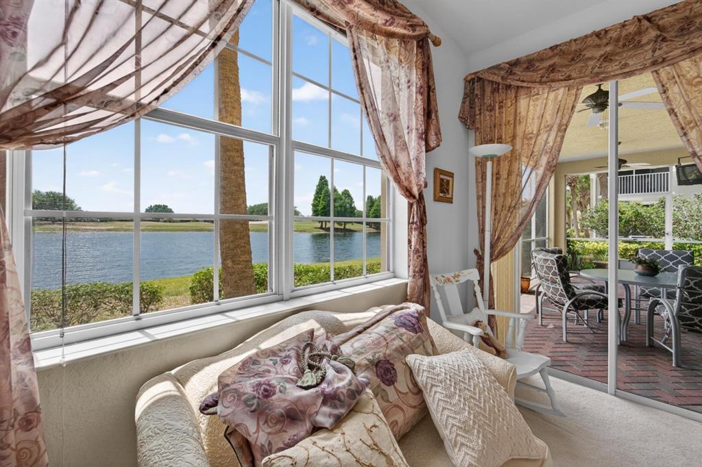 A sunroom with a sofa, floral curtains, and a view of a lake and patio — 1364 EMERALD DUNES DRIVE, SUN CITY CENTER, FL