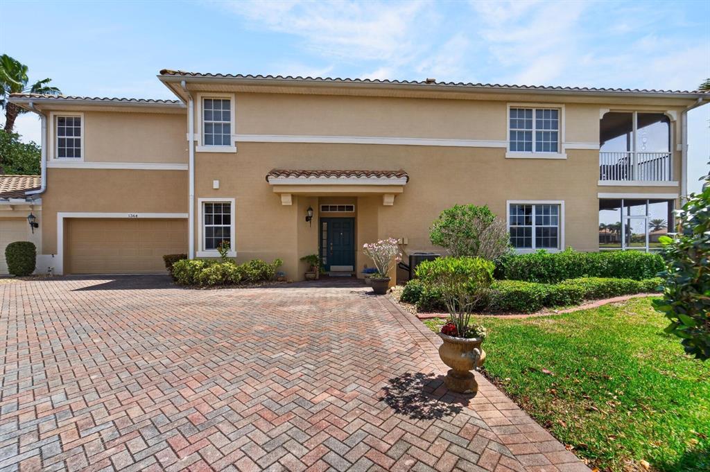 A two-story house with a beige stucco exterior, a brick driveway, and a tiled roof — 1364 EMERALD DUNES DRIVE, SUN CITY CENTER, FL