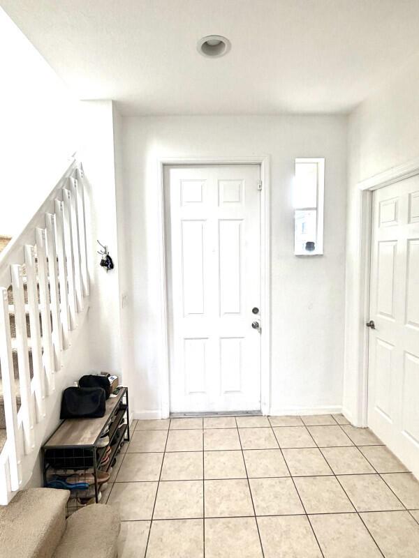 An entryway features a white front door, tiled flooring, and a staircase with white railings — 1205 Abaco Lane, Riviera Beach FL 33404, RIVIERA BEACH, FL