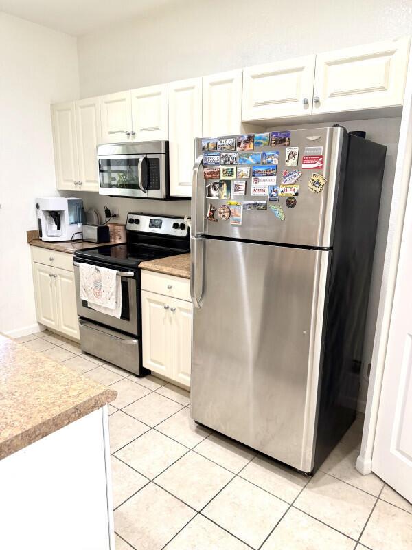 A kitchen features white cabinetry, stainless steel appliances, and a refrigerator covered in magnets — 1205 Abaco Lane, Riviera Beach FL 33404, RIVIERA BEACH, FL