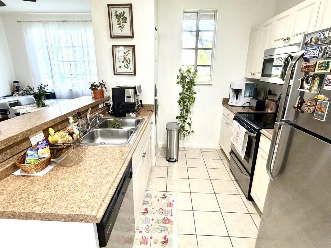 A kitchen features light-colored cabinets, tan laminate countertops, stainless steel appliances, and tile flooring — 1205 Abaco Lane, Riviera Beach FL 33404, RIVIERA BEACH, FL