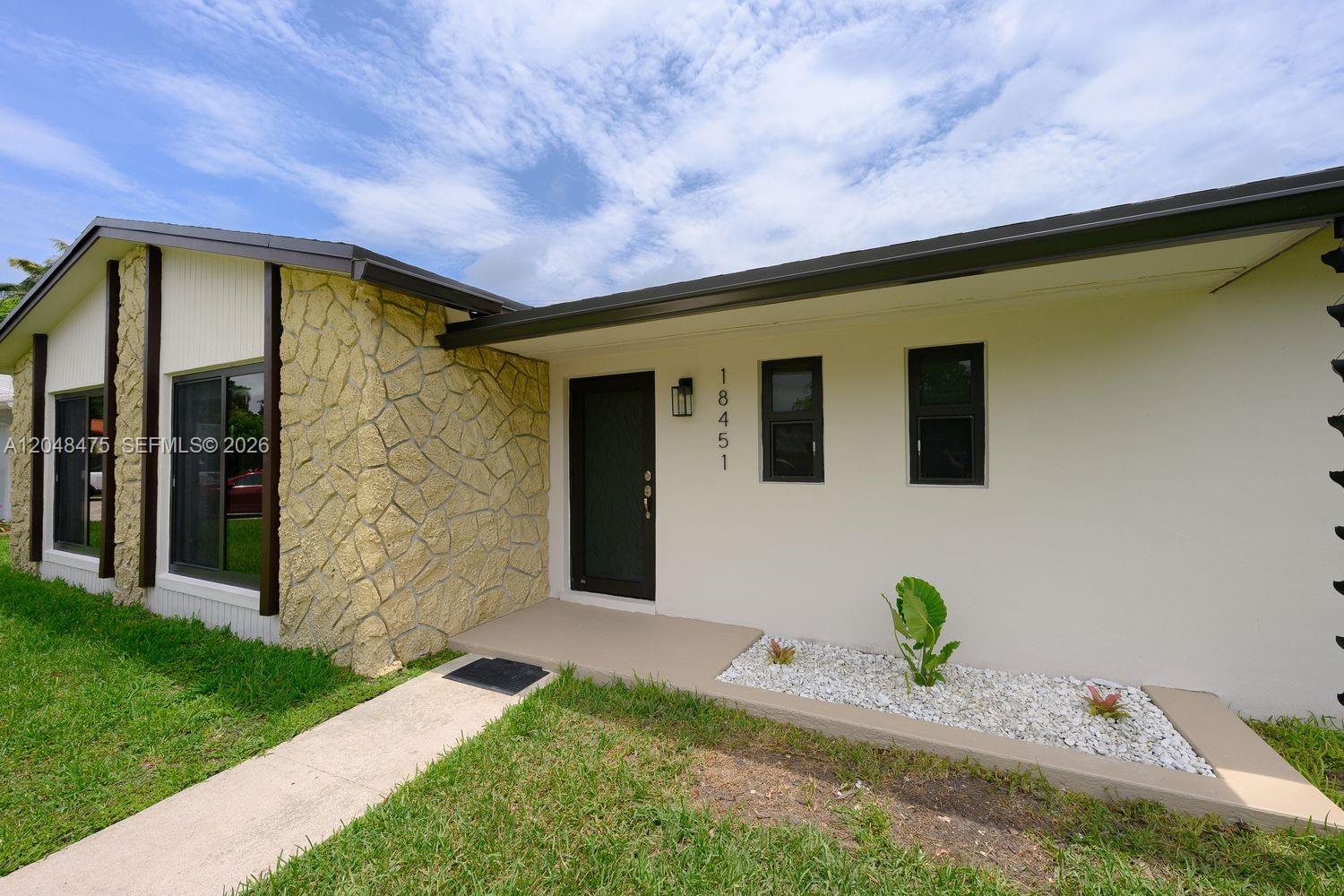 The exterior of a house features a stone facade, a dark front door, and windows — 18451 SW 90th Ave, Cutler Bay FL 33157, CUTLER BAY, FL