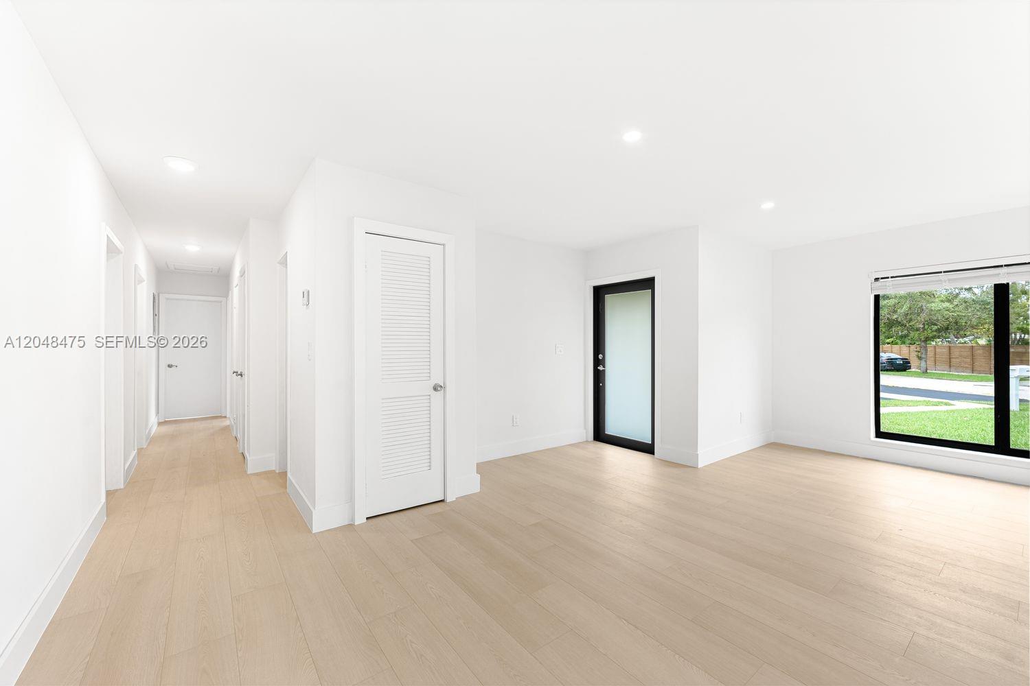 A bright, minimalist room features light wood flooring, white walls, and a black-framed glass door — 18451 SW 90th Ave, Cutler Bay FL 33157, CUTLER BAY, FL
