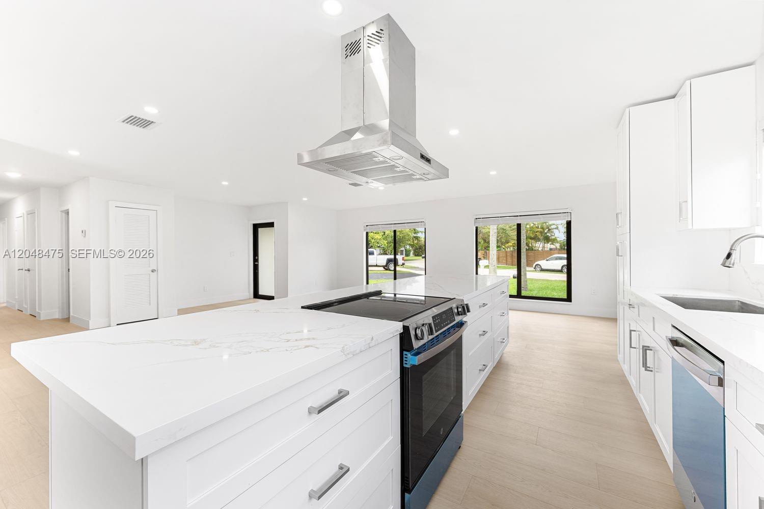 A modern white kitchen features a large island with a cooktop and range hood — 18451 SW 90th Ave, Cutler Bay FL 33157, CUTLER BAY, FL