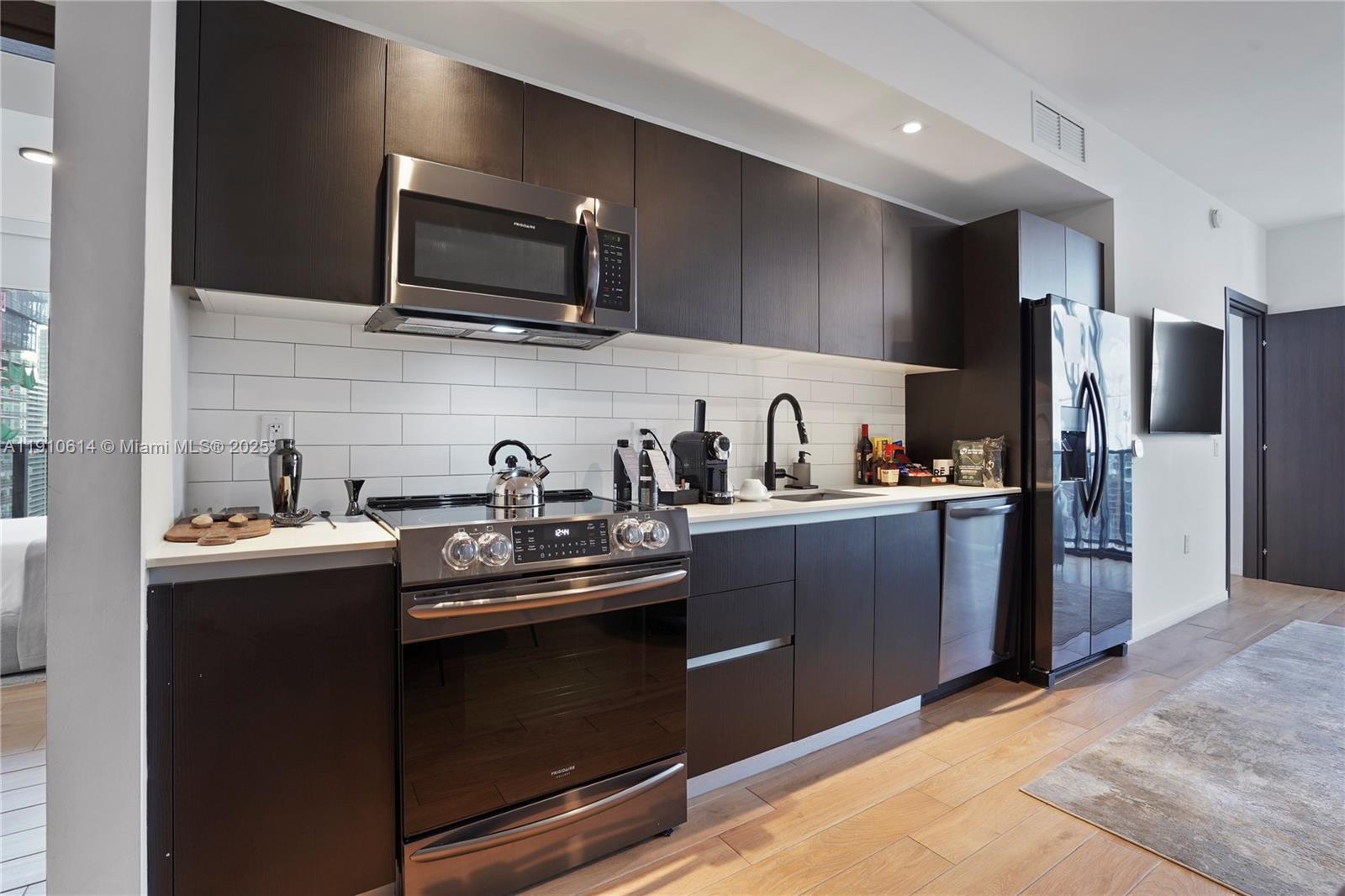A modern kitchen features dark wood cabinetry, stainless steel appliances, and a white subway tile backsplash — 398 NE 5th St # 3618, Miami FL 33132, MIAMI, FL