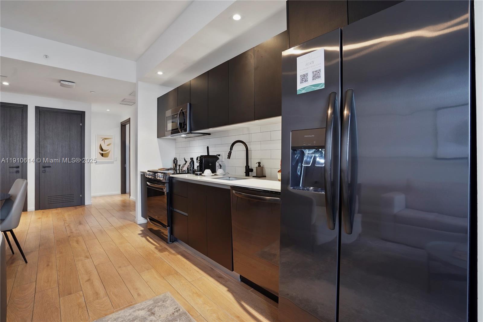 A modern kitchen features dark cabinetry, stainless steel appliances, and light wood flooring — 398 NE 5th St # 3618, Miami FL 33132, MIAMI, FL