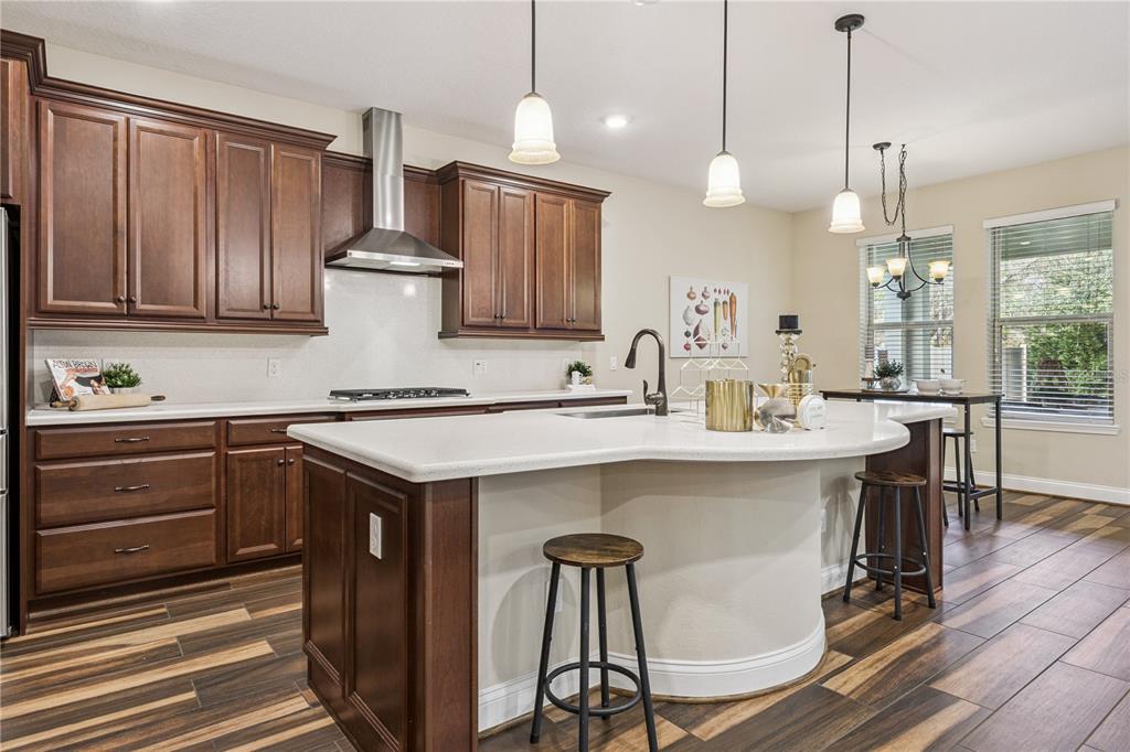 A kitchen features dark wood cabinets, a curved white island with stools, and wood-look flooring — 13525 GORGONA ISLE DRIVE, WINDERMERE, FL