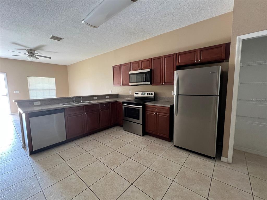 A kitchen features dark wood cabinets, stainless steel appliances, granite countertops, and light tile flooring — 832 ABBEVILLE COURT UNIT A, KISSIMMEE, FL