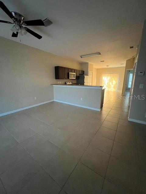 An open-concept kitchen with dark cabinets and a breakfast bar overlooks a tiled living area — 832 ABBEVILLE COURT UNIT A, KISSIMMEE, FL