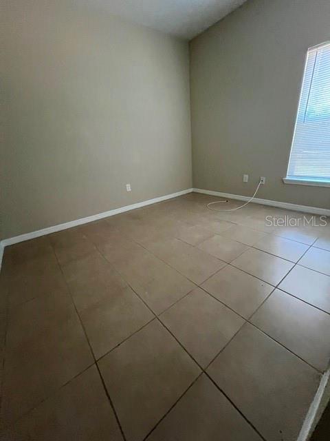 An empty room features light-colored walls, large beige floor tiles, and a window with blinds — 832 ABBEVILLE COURT UNIT A, KISSIMMEE, FL