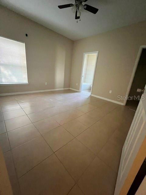 An empty room with beige tile flooring, a ceiling fan, and a doorway to a bathroom — 832 ABBEVILLE COURT UNIT A, KISSIMMEE, FL