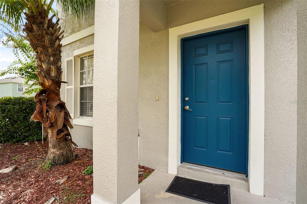 A blue front door sits under a covered entryway next to a palm tree — 14837 HUNTLEY DRIVE, ORLANDO, FL