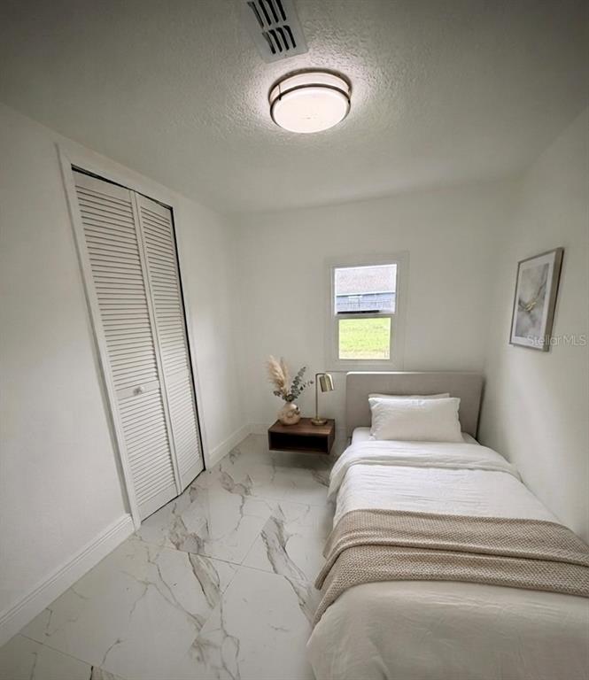 A small bedroom features white walls, marble-patterned tile flooring, a single bed, and a closet — 5228 ANDRUS AVENUE, ORLANDO, FL