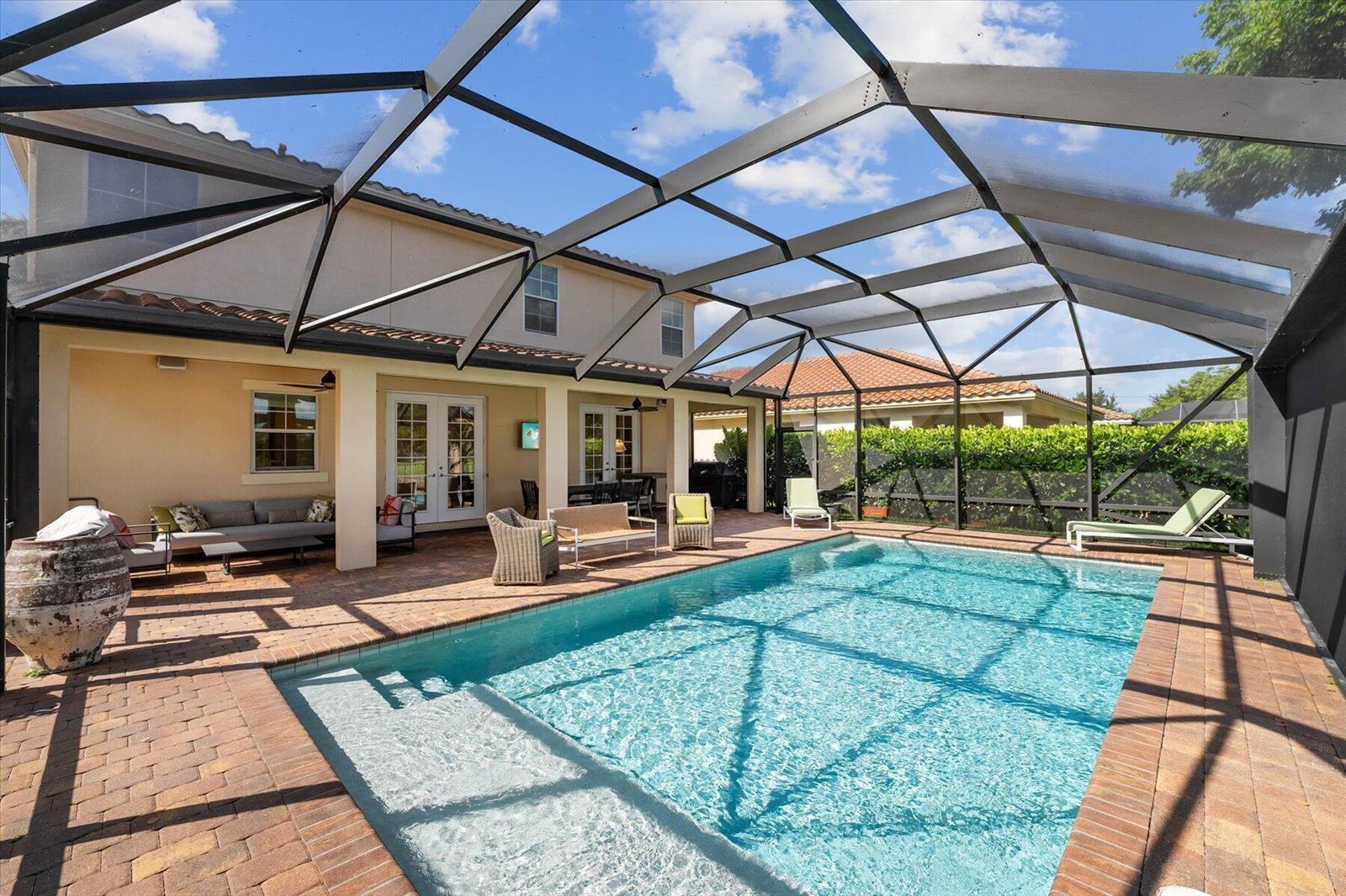 A screened-in patio features a rectangular swimming pool, brick pavers, and outdoor furniture — 10731 Ivanhoe Lane, Wellington FL 33414, WELLINGTON, FL