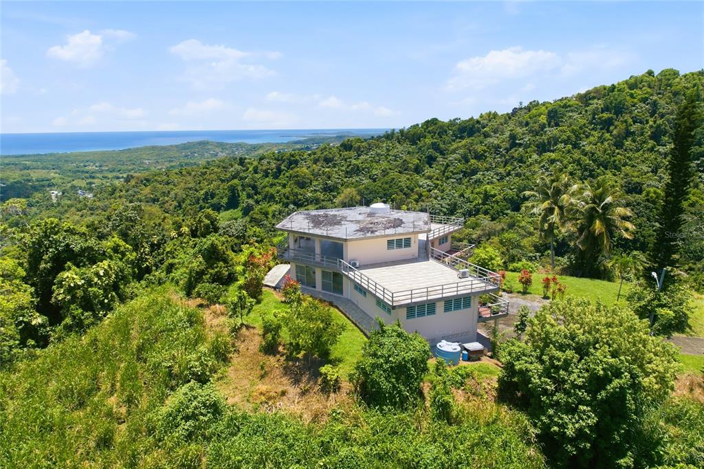 An aerial view shows a multi-level house with flat roofs surrounded by dense tropical forest — 988 KM 1.5, LUQUILLO, PR