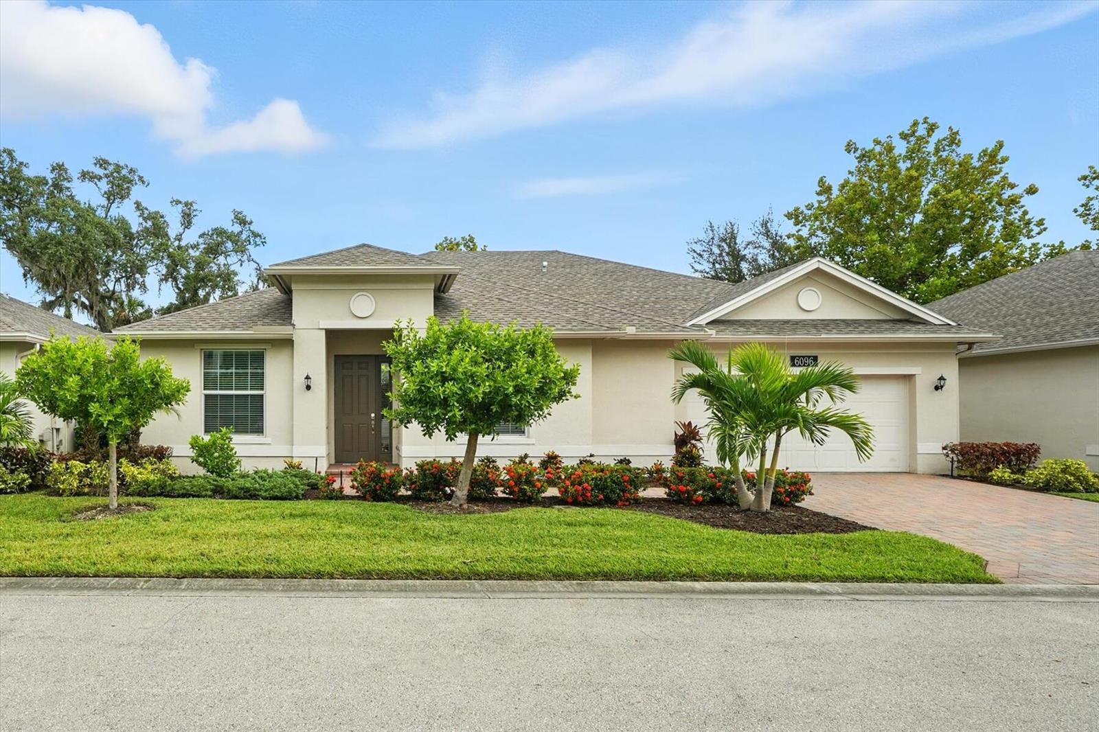 A single-story house with a beige exterior, a paved driveway, and a landscaped front yard — 6096 Bella Rosa Lane, Vero Beach FL 32966, VERO BEACH, FL