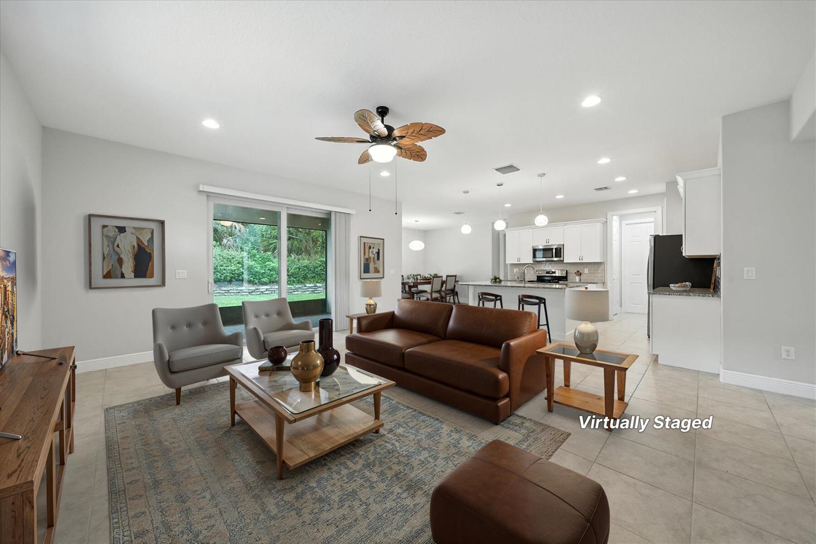 A virtually staged open-concept living room and kitchen featuring tile floors and a leather sofa — 6096 Bella Rosa Lane, Vero Beach FL 32966, VERO BEACH, FL