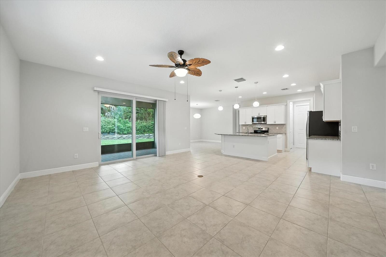 An open-concept living area with tile flooring, a kitchen island, and sliding glass patio doors — 6096 Bella Rosa Lane, Vero Beach FL 32966, VERO BEACH, FL