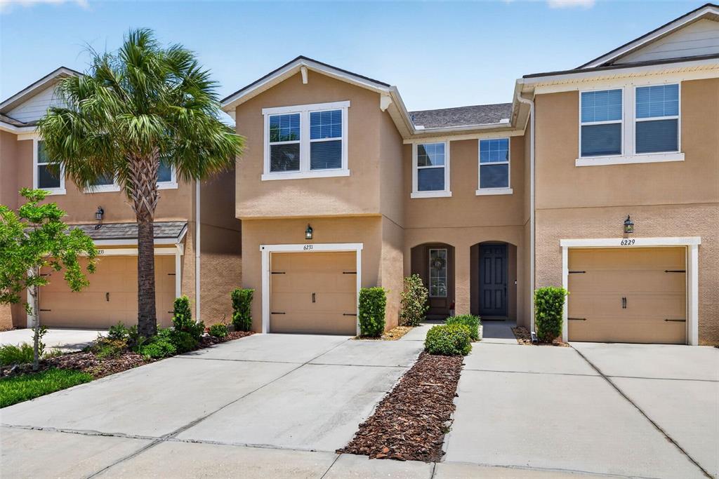 A tan two-story townhouse features a garage, a front door, and a palm tree — 6231 SCARLET DARTER WAY, TAMPA, FL
