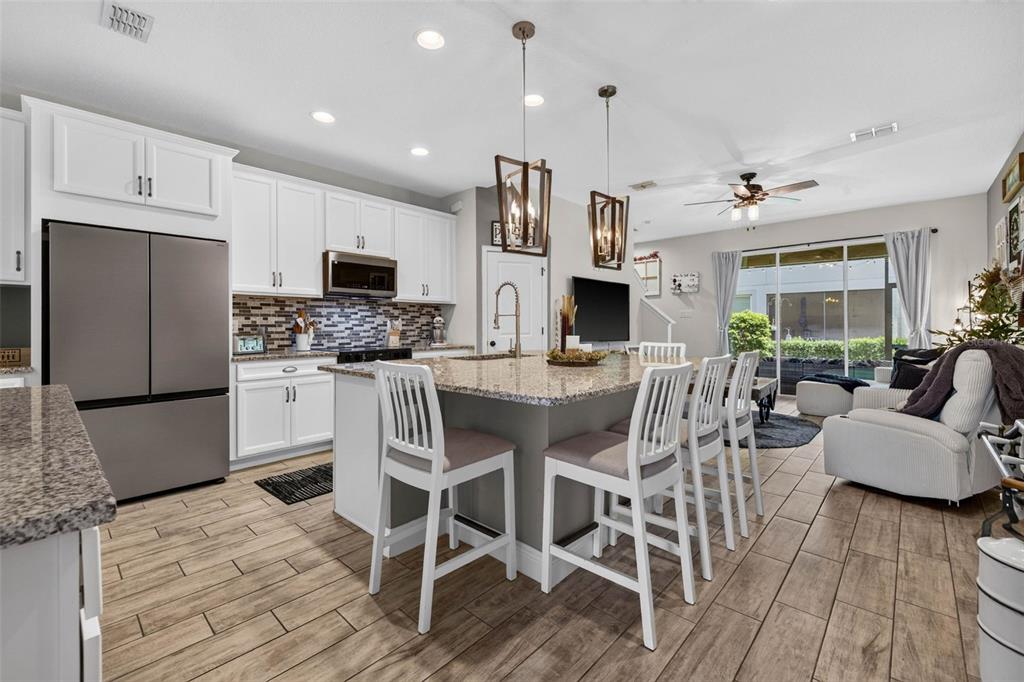 A kitchen with white cabinets, granite countertops, a central island, and wood-look tile flooring — 6231 SCARLET DARTER WAY, TAMPA, FL