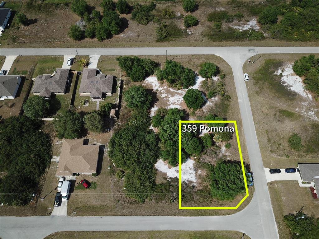 An aerial view shows a vacant, tree-covered corner lot outlined in yellow near residential houses — 359 POMONA STREET, LEHIGH ACRES, FL