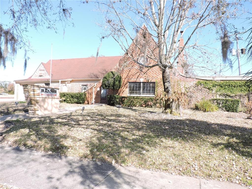 A brick building with a steep roof and a stone sign stands near a tree — 322 SCENIC HIGHWAY N, LAKE WALES, FL