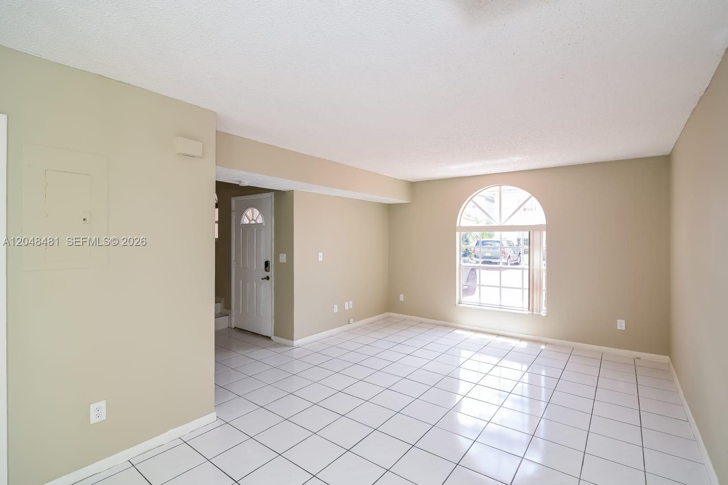 An empty room features white tiled floors, beige walls, and an arched window — HIALEAH, FL