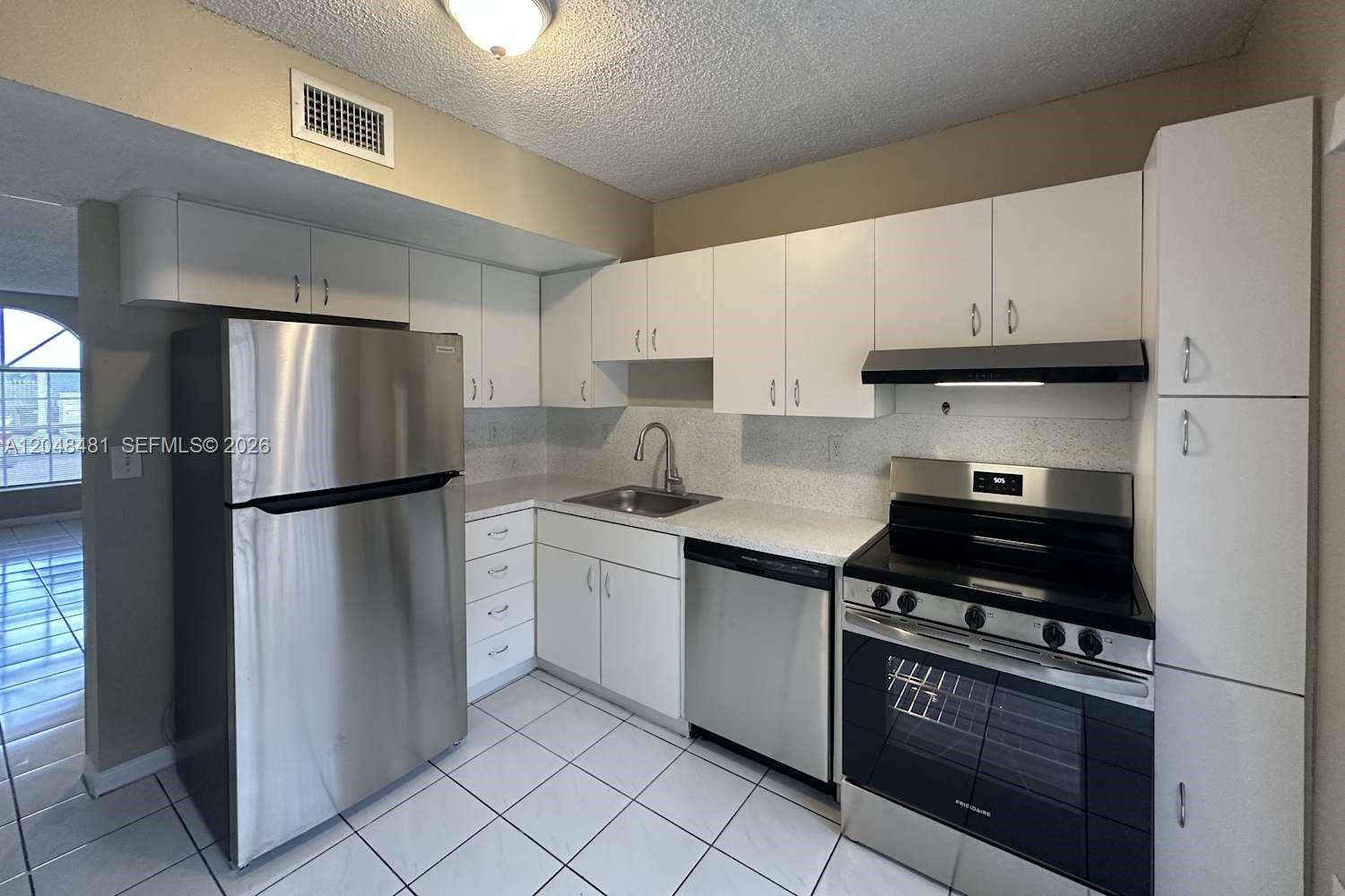 A kitchen features white cabinets, stainless steel appliances, and white tile flooring — HIALEAH, FL
