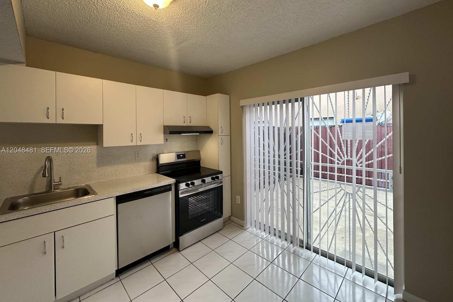 A kitchen features white cabinets, stainless steel appliances, tile flooring, and a sliding glass door — HIALEAH, FL