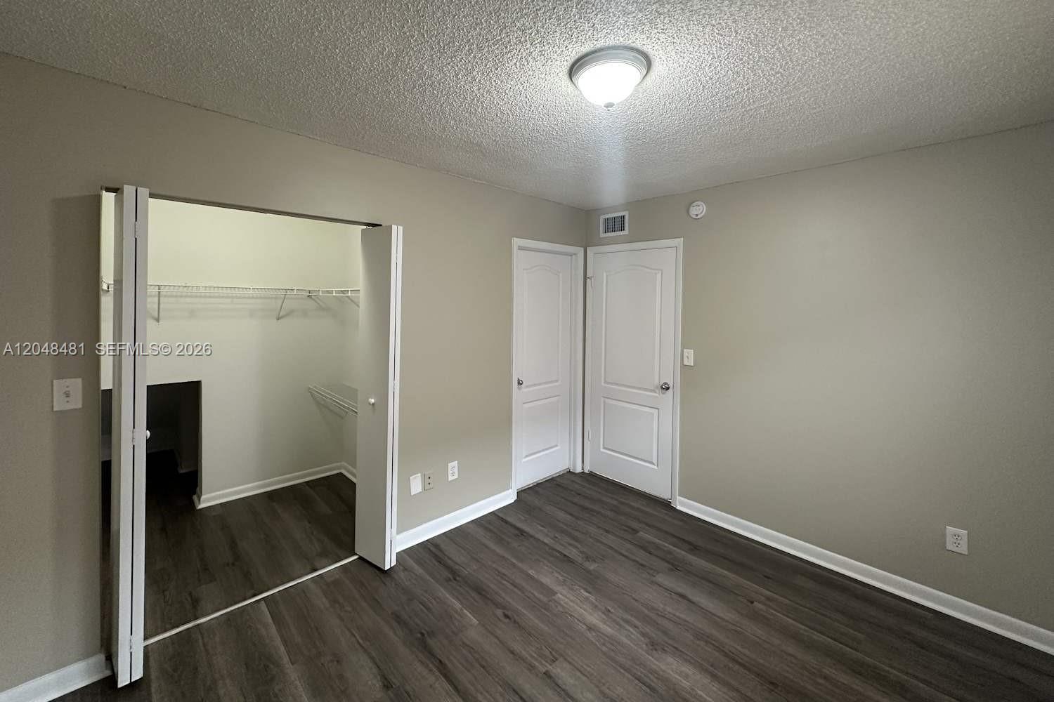 A bedroom features gray walls, wood-look flooring, a walk-in closet, and two white doors — HIALEAH, FL