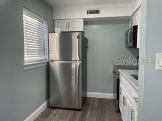 A kitchen features stainless steel appliances, white cabinets, and light gray walls over wood flooring — 416 MONROE AVENUE UNIT F201, CAPE CANAVERAL, FL