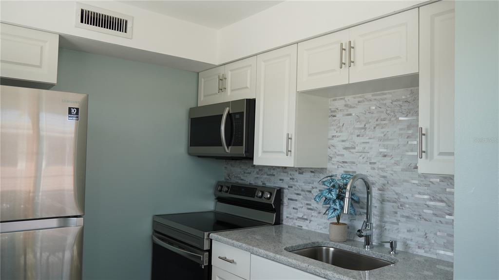 A kitchen features white cabinets, stainless steel appliances, granite countertops, and a mosaic tile backsplash — 416 MONROE AVENUE UNIT F201, CAPE CANAVERAL, FL