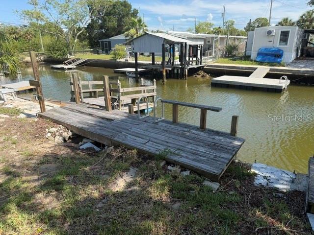 A wooden dock extends into a canal with a covered boat slip and nearby house — 6832 ALBATROSS LANE, HUDSON, FL