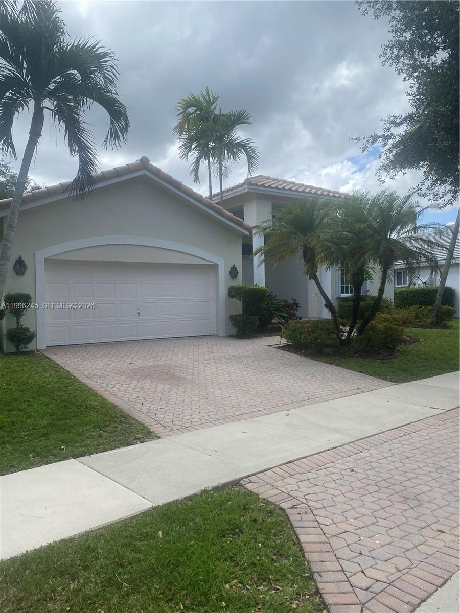 A single-story house features a two-car garage, a paved driveway, and several palm trees — 3066 Lakewood Cir, Weston FL 33332, WESTON, FL