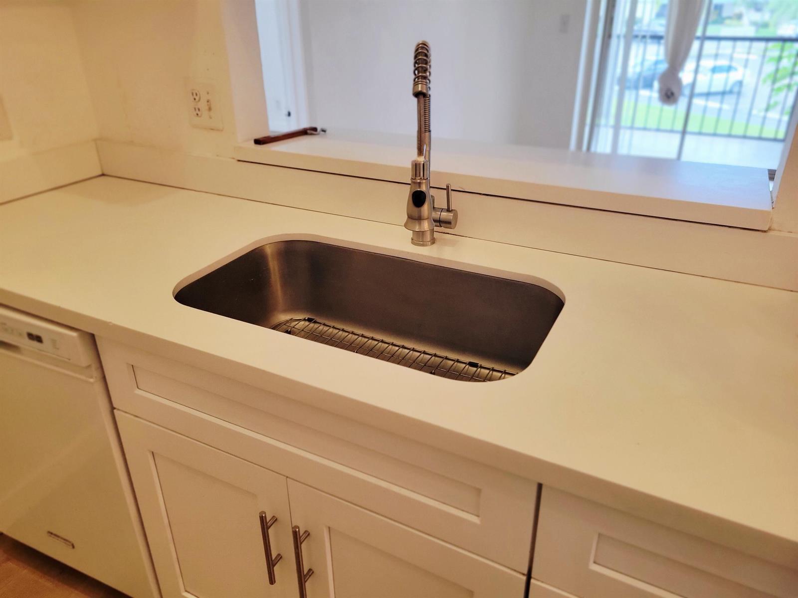 A stainless steel kitchen sink with a gooseneck faucet is set in white countertops — 6285 Chasewood Drive # F, Jupiter FL 33458, JUPITER, FL