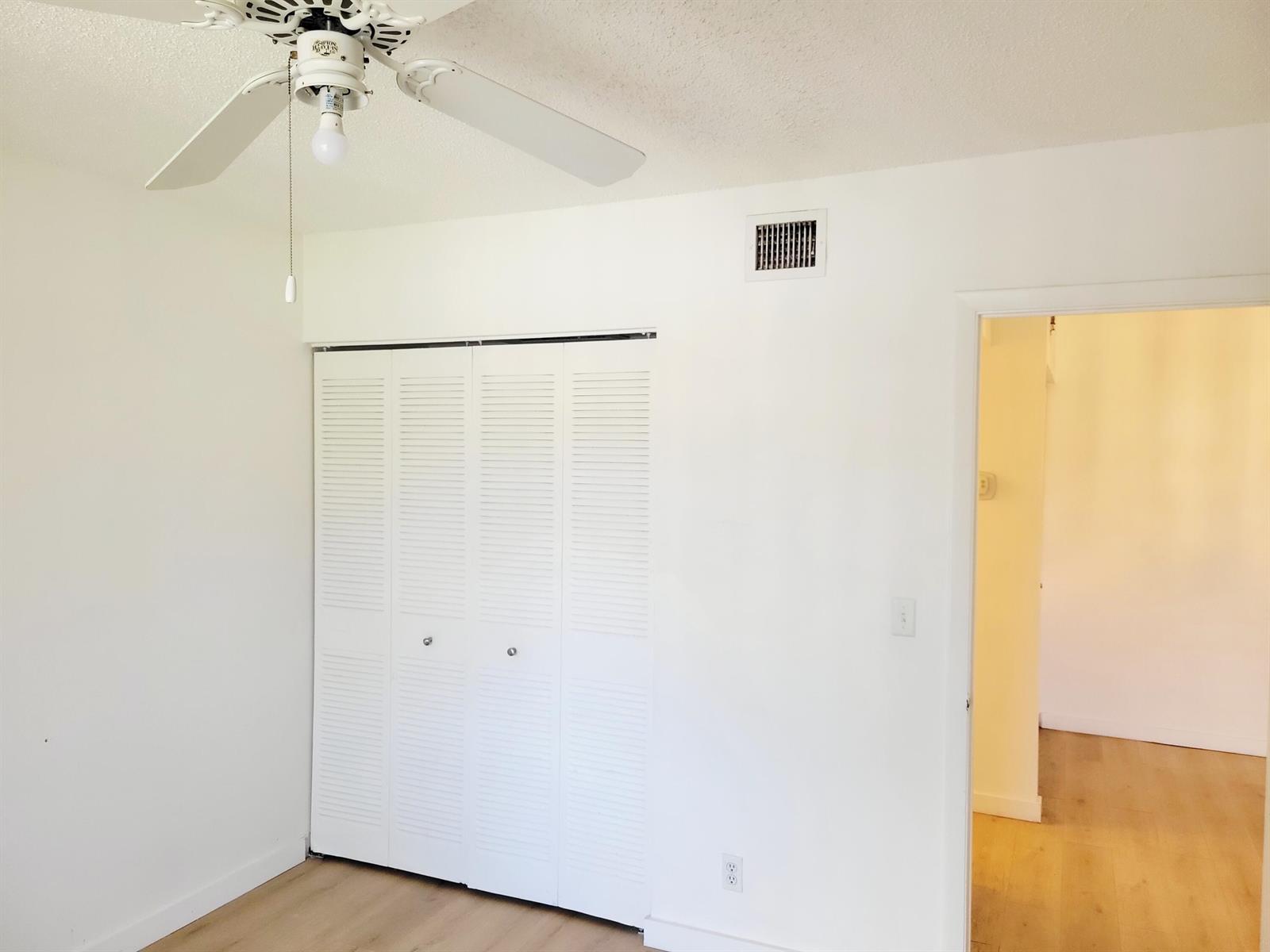 A bedroom features white walls, light wood flooring, a ceiling fan, and a louvered closet — 6285 Chasewood Drive # F, Jupiter FL 33458, JUPITER, FL